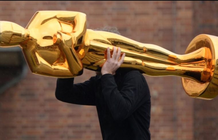 Un acteur tient fièrement une statue d'Oscar en or au-dessus de sa tête.