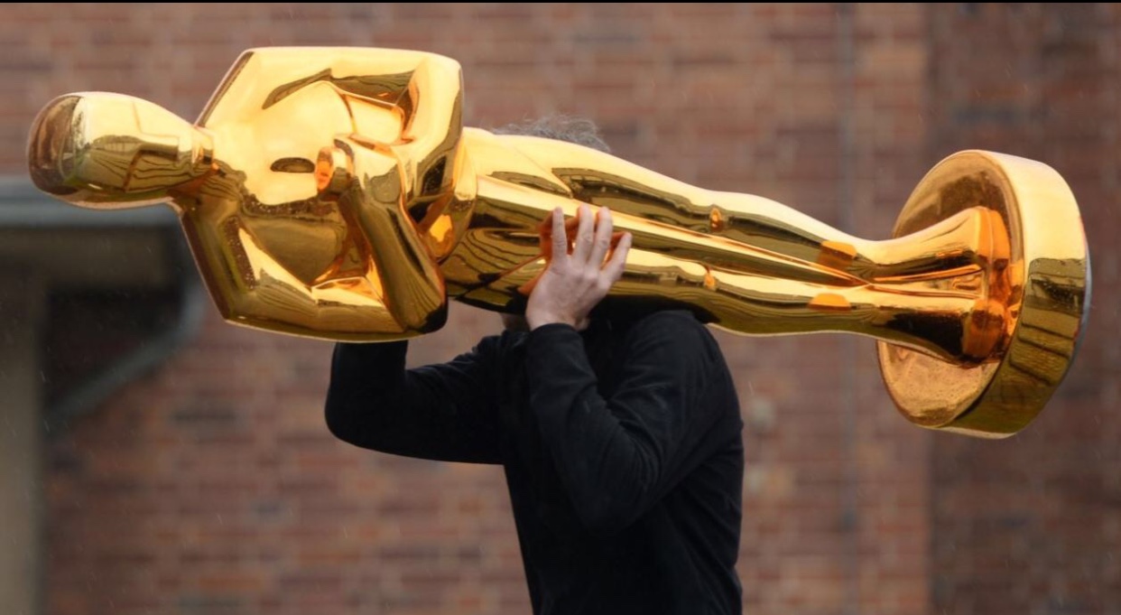 Un acteur tient fièrement une statue d'Oscar en or au-dessus de sa tête.