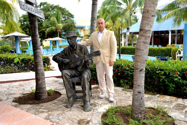 Un homme debout à côté d'une statue représentant un homme jouant de la guitare à Holguin pendant ses vacances.