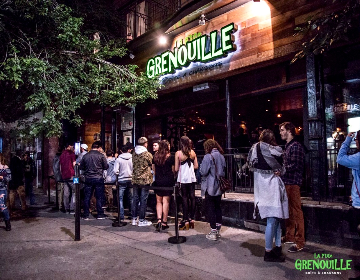 Un groupe de personnes debout devant le restaurant La Petite Grenouille la nuit.