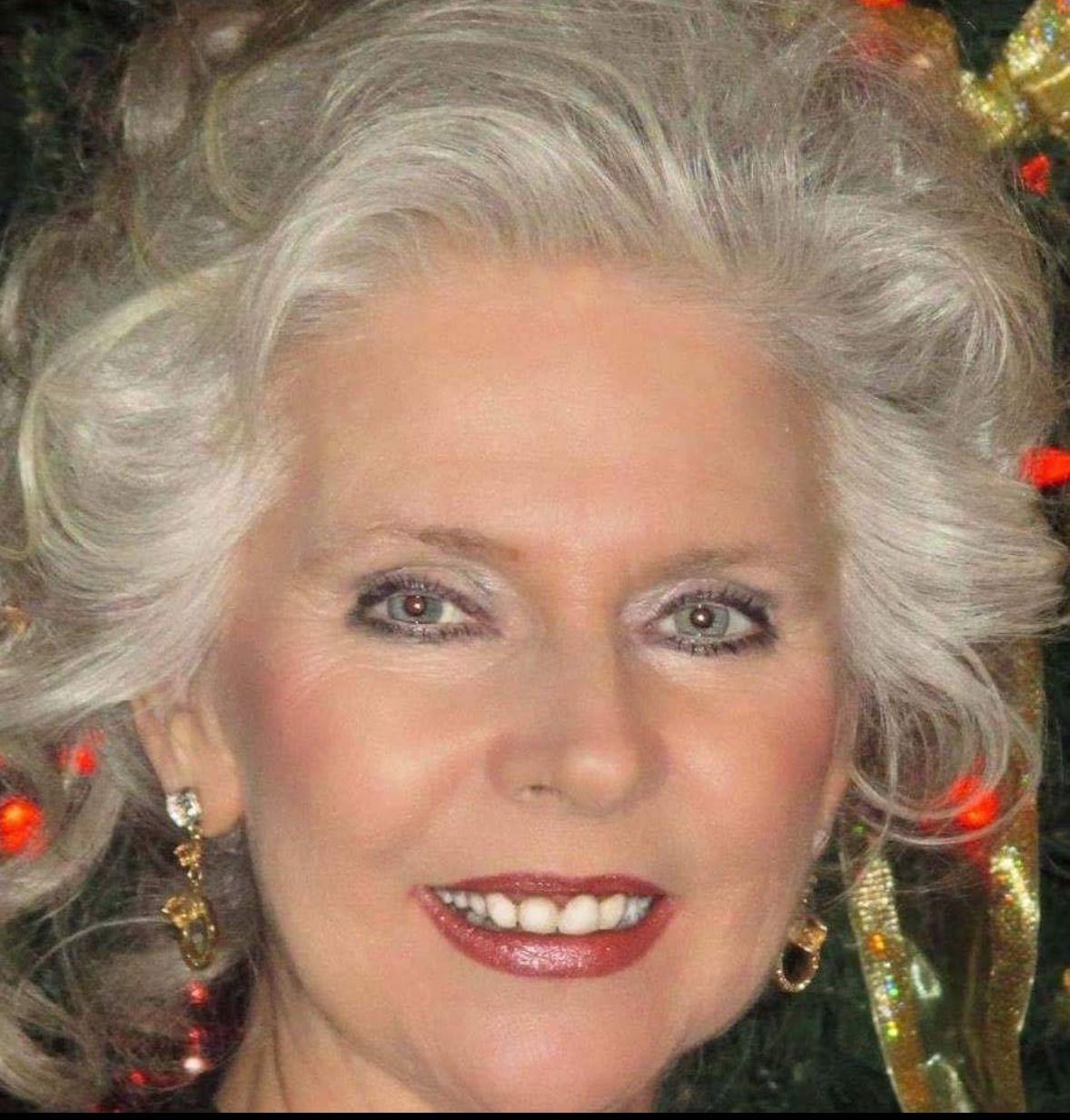 Une femme aux cheveux gris souriant devant un sapin de Noël, représentant la joie du temps des fêtes.