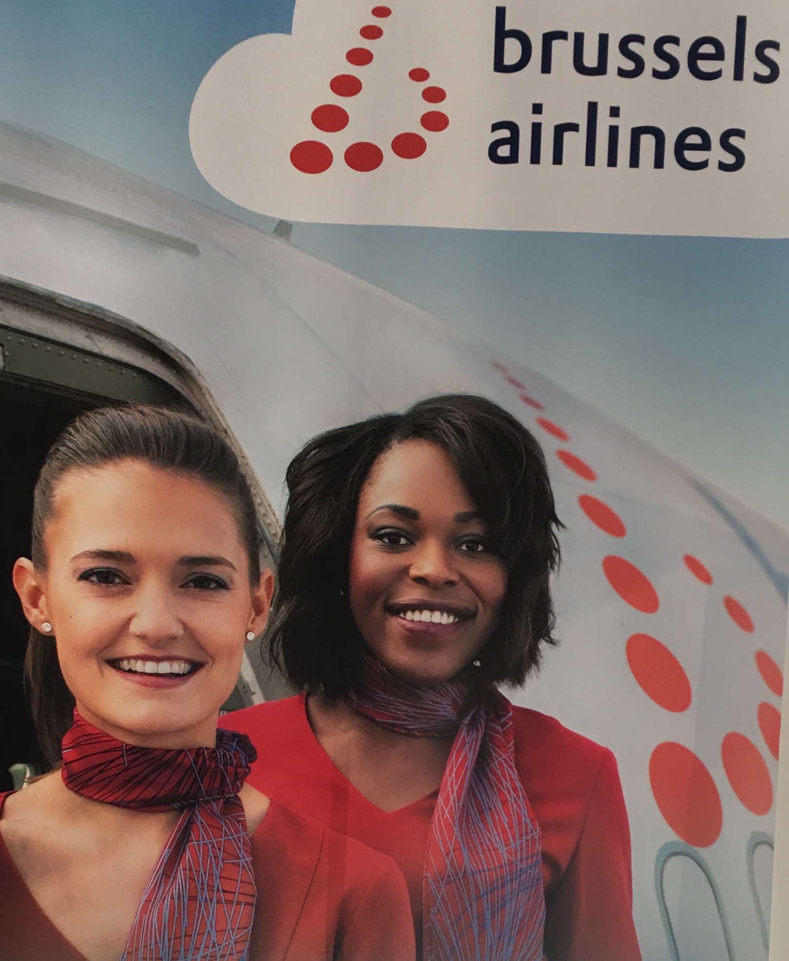 Deux agents de bord de Brussels Airlines debout devant une pancarte invitant les voyageurs à découvrir l'Afrique de l'Ouest.