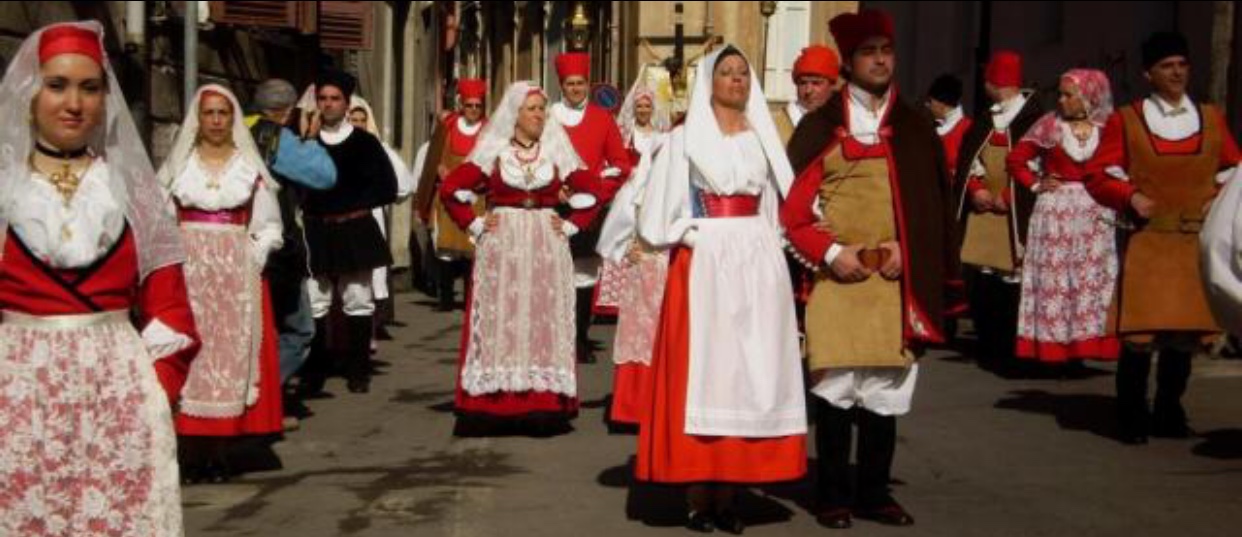 Un groupe de personnes habillées dans la tradition de La Sardaigne marchent dans une rue, représentant la vitalité vibrante de leur culture.