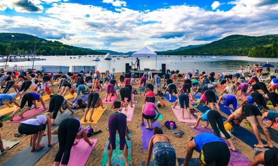 Un groupe de personnes pratiquant le yoga sur une plage près d’un lac, embrassant l’esprit du voyage.