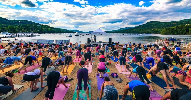 Un groupe de personnes pratiquant le yoga sur une plage près d’un lac, embrassant l’esprit du voyage.