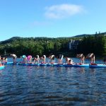 Un groupe de passionnés de Wanderlust pratiquant le yoga sur des planches à pagaie dans un lac.