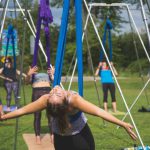 Un groupe de personnes pratiquant le yoga aérien dans un parc, exprimant leur envie de voyager à travers des inversions et des poses.