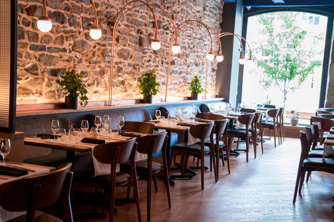 Chez L'Épicier, un restaurant avec mur de pierre et tables en bois.