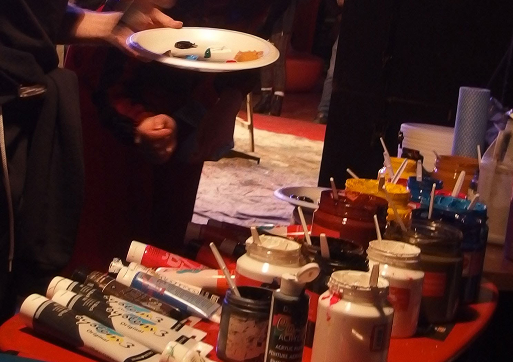 Lors d'un événement artistique, un homme tient un plateau de peintures, prêt à créer des chefs-d'œuvre.