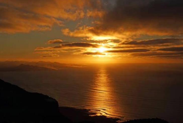 La créatrice contemple la spiritualité du soleil qui se couche sur l'océan depuis le sommet d'une montagne.