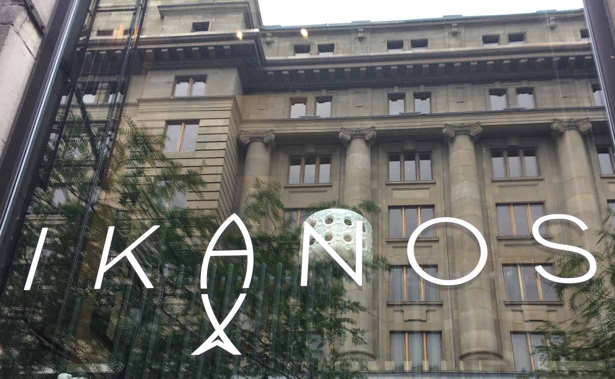 Un panneau indiquant « Ikanos » devant un bâtiment, mettant en valeur le mot grec signifiant « poisson » (poisson grec) pendant la journée.