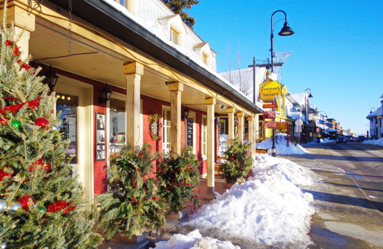 Baie St-Paul, une petite ville nichée au milieu de terres fertiles, présente une scène pittoresque avec des arbres de Noël ornés de lumières scintillantes et un trottoir recouvert de neige immaculée. Celui de la ville