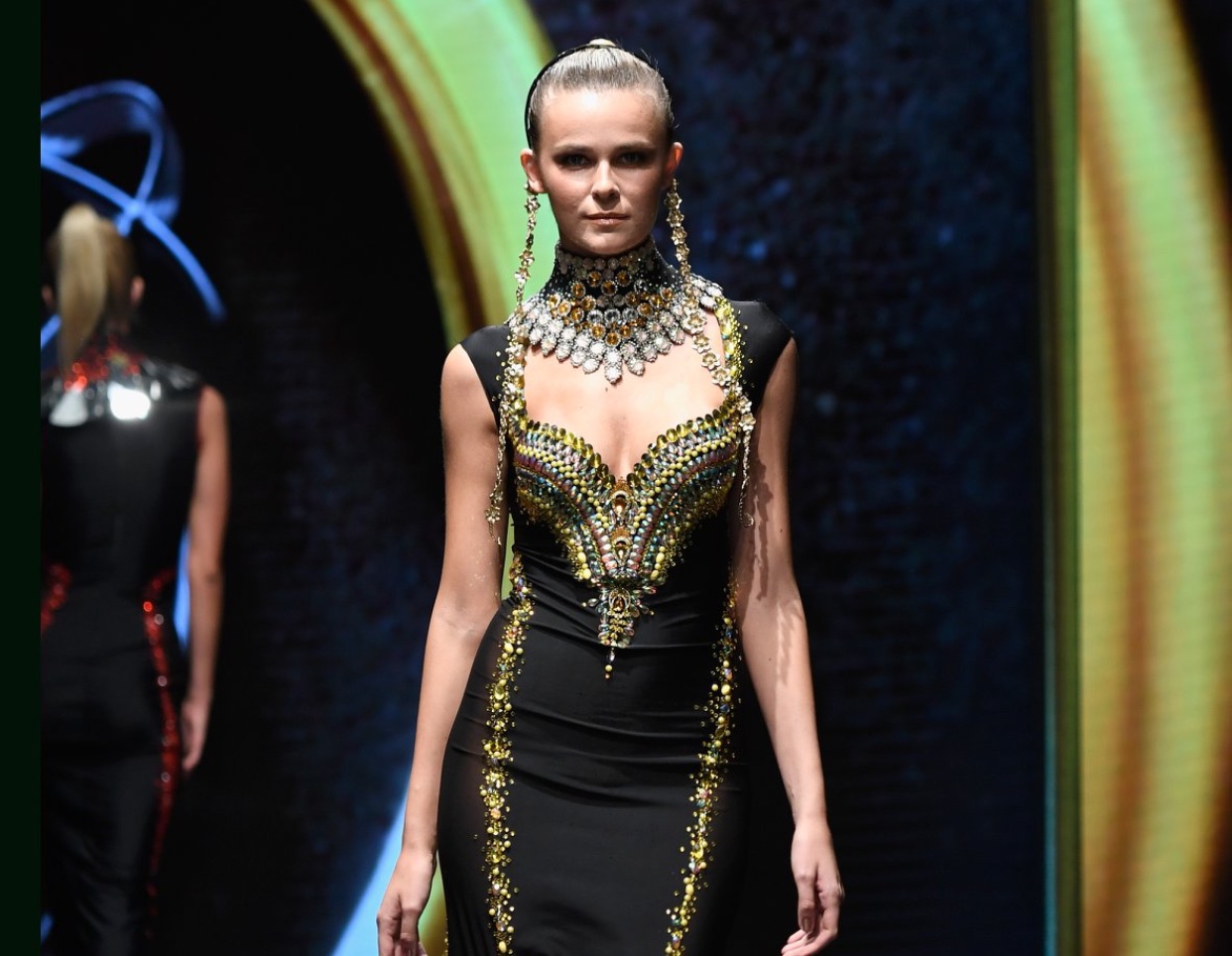 Un mannequin défile lors de la Cosmopolitan Fashion Week dans une robe glamour noire et dorée.