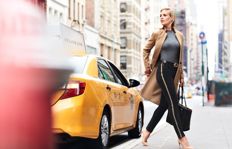 Mélanie Lyne, une femme marchant dans une rue de la ville avec un taxi en arrière-plan.