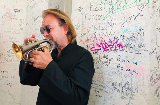 Un homme jouant de la trompette devant un mur recouvert de graffitis.
