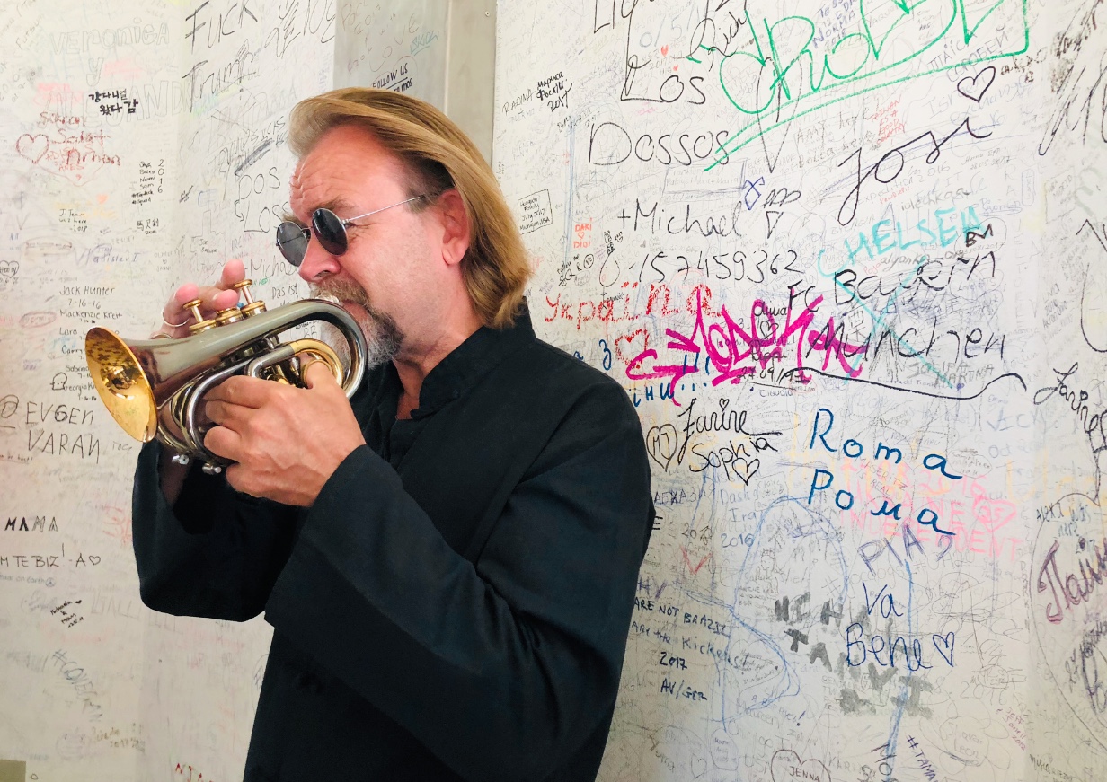 Un homme jouant de la trompette devant un mur recouvert de graffitis.