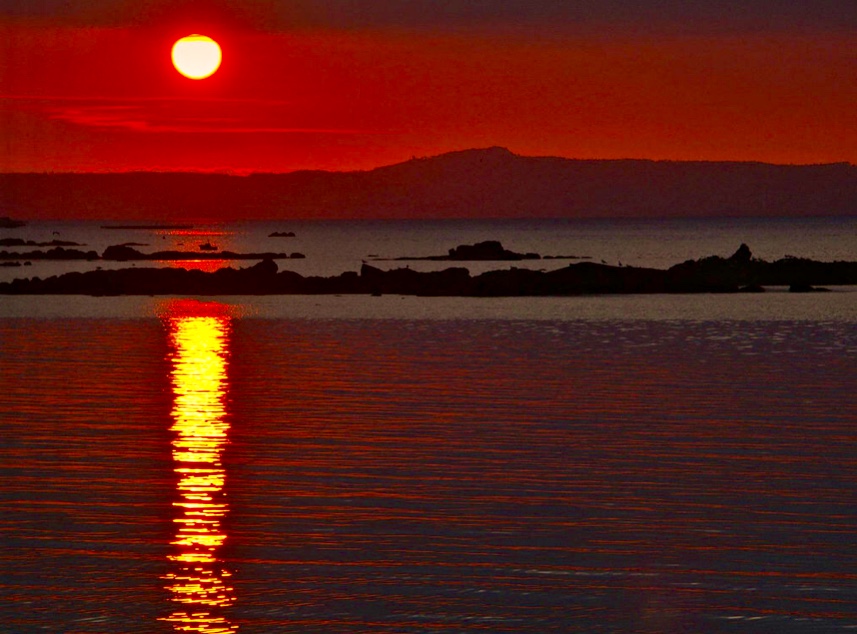 Un soleil rouge, symbolisant la spiritualité, se couchant sur un plan d'eau serein.