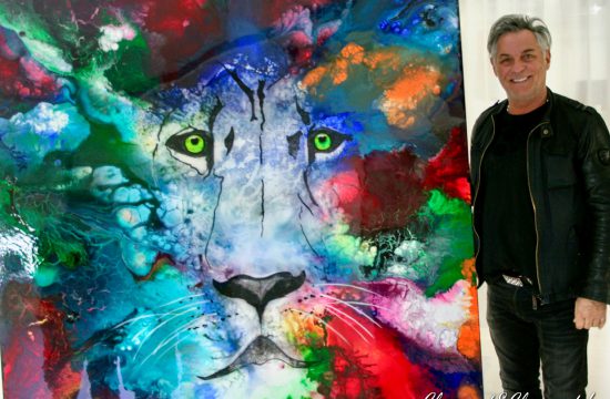 Un homme, Riccio, debout à côté d’une peinture colorée représentant un lion.