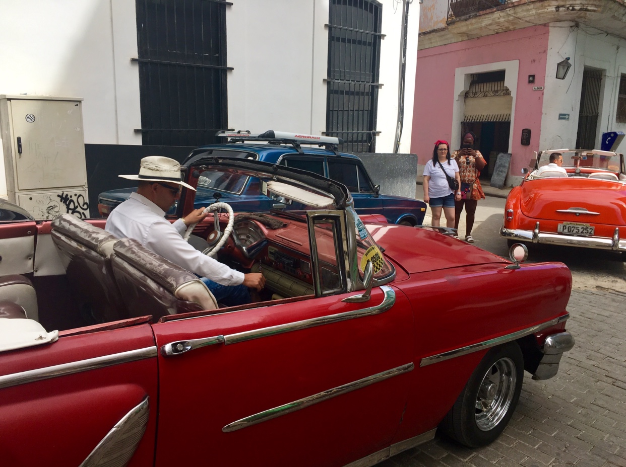 Un homme conduit une voiture classique rouge à travers La Havane.