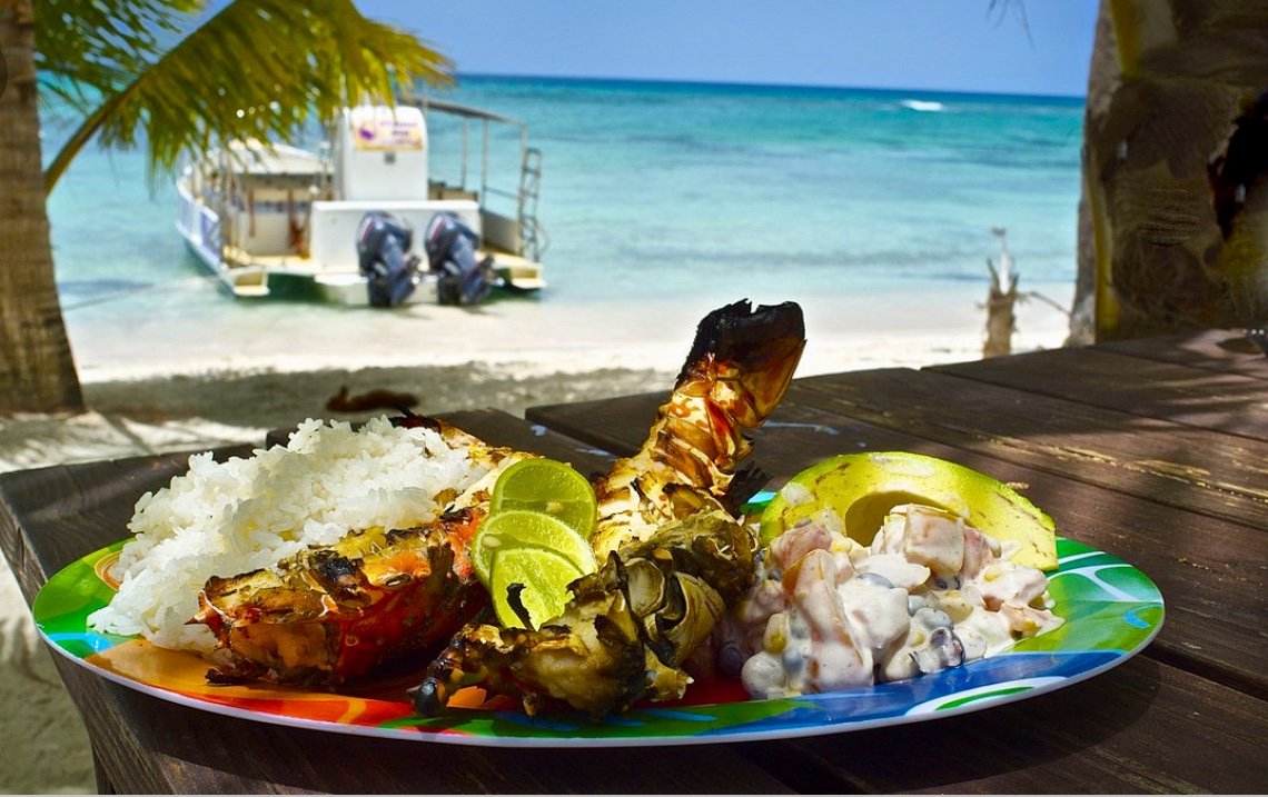 Une assiette de nourriture sur une table à côté d'un bateau sur la plage de La République Dominicaine.