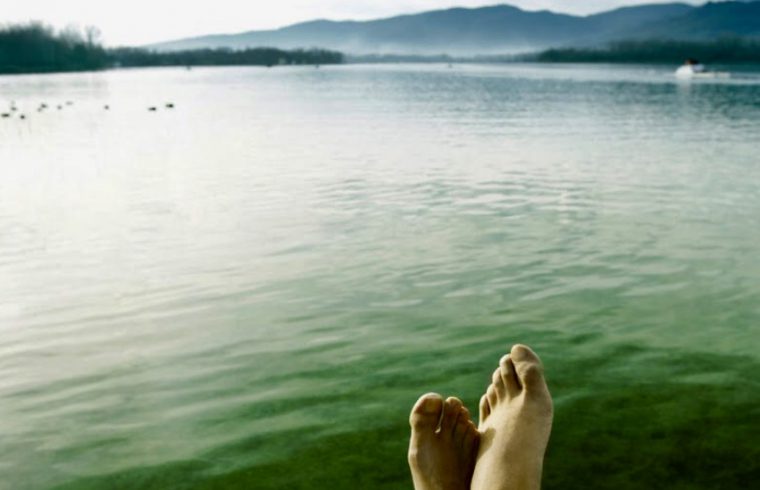 Les pieds d'une personne sur un quai surplombant un lac serein, expérimentant le mélange tranquille de spiritualité et d'inspiration créative.