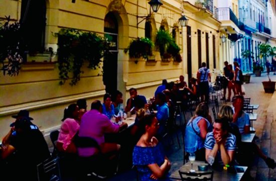 Un groupe de personnes assises à des tables dans une rue étroite de Cuba.
