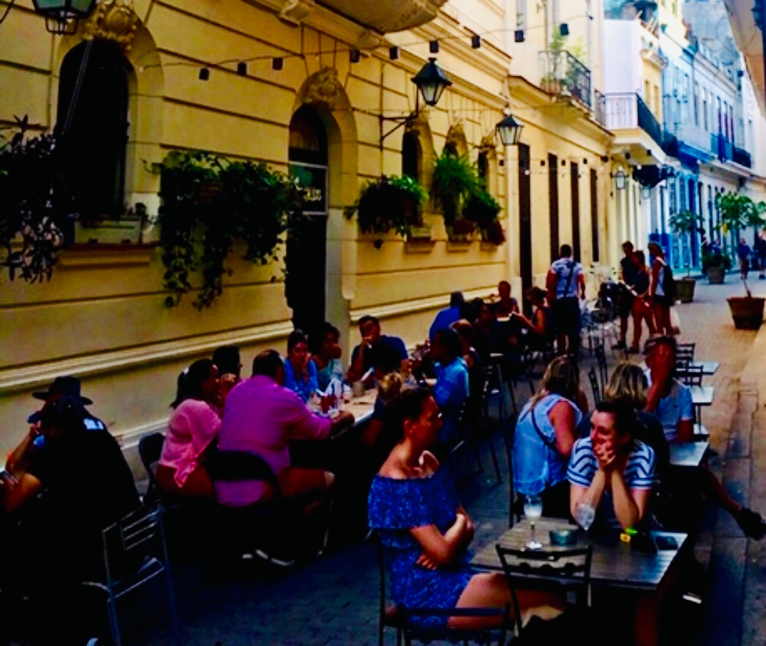 Un groupe de personnes assises à des tables dans une rue étroite de Cuba.