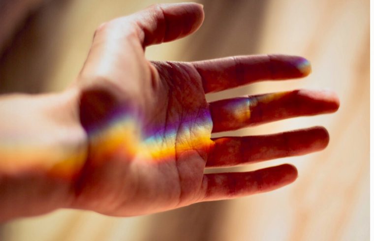 La main d'une personne avec un arc-en-ciel aux couleurs vives qui s'y reflète, respirant la spiritualité et la créativité.