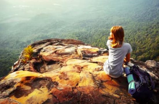 La spiritualité : Une femme assise au sommet d'un rocher contemplant une vallée.