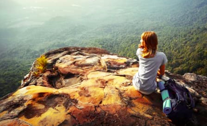 La spiritualité : Une femme assise au sommet d'un rocher contemplant une vallée.