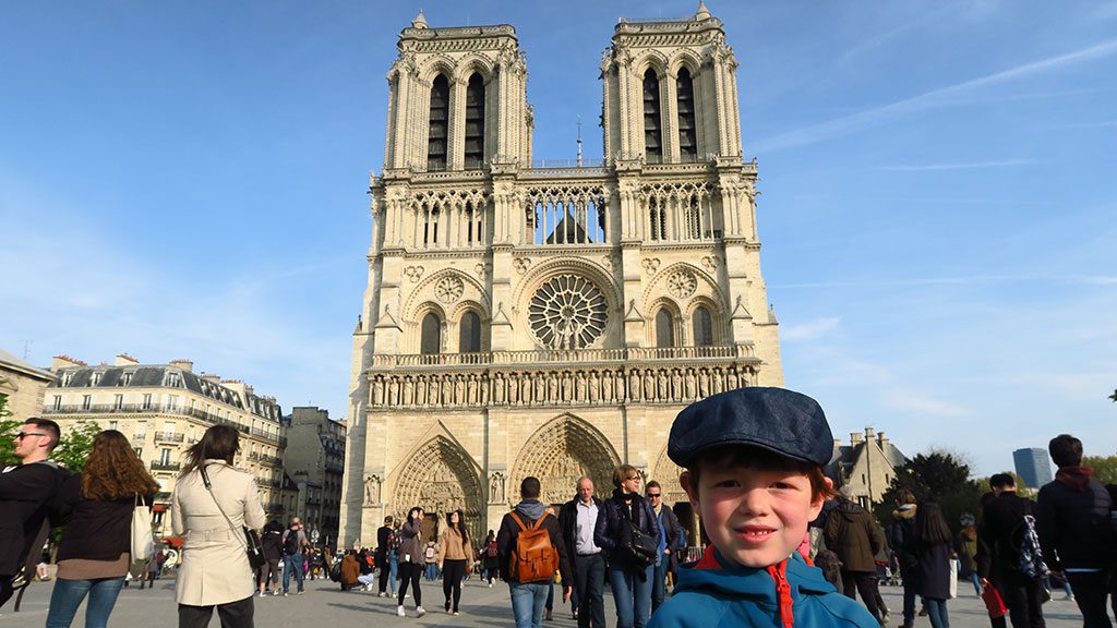 Un jeune garçon se tient devant Notre-Dame de Paris, une grande cathédrale.
