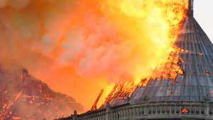 Notre-Dame de Paris, un grand édifice, est en feu et des flammes en sortent.