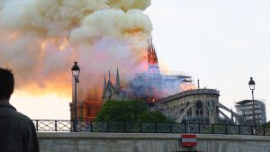 Un homme se tient devant Notre-Dame de Paris et de la fumée s'en échappe.