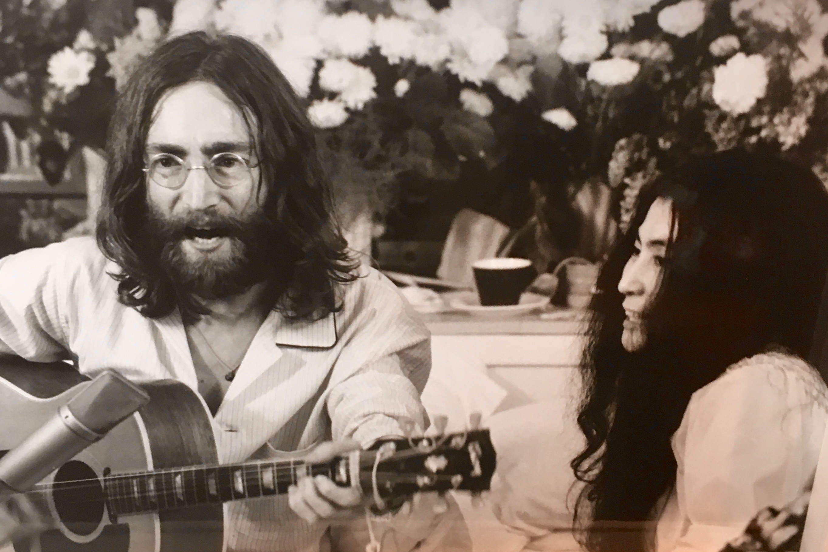 Une photo en noir et blanc de John Lennon et d'une femme jouant d'une guitare acoustique prise lors de l'événement Sortir à Montréal.
