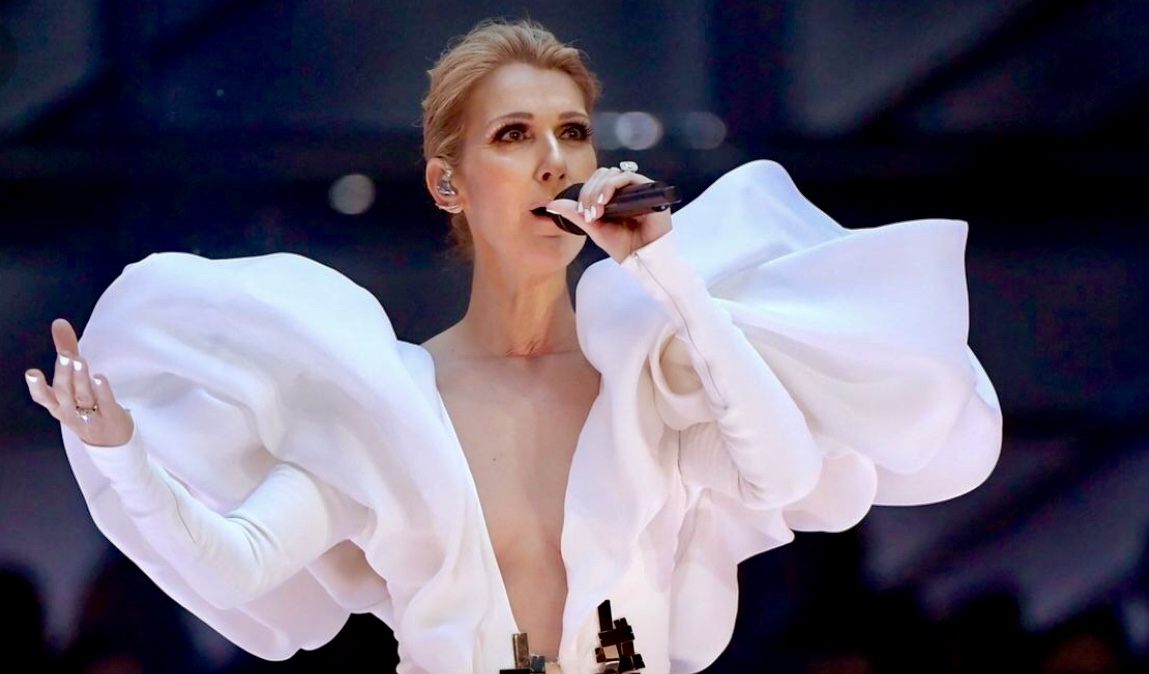 Céline Dion, vêtue d'une robe blanche, chante de manière captivante dans un micro.