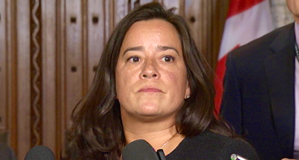 Une femme se tient devant des micros pour parler du scandale SNC-LAVALIN, avec le drapeau canadien en toile de fond.