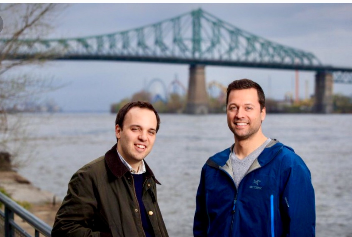 Deux hommes debout devant le fleuve Saint-Laurent avec un pont en arrière-plan.