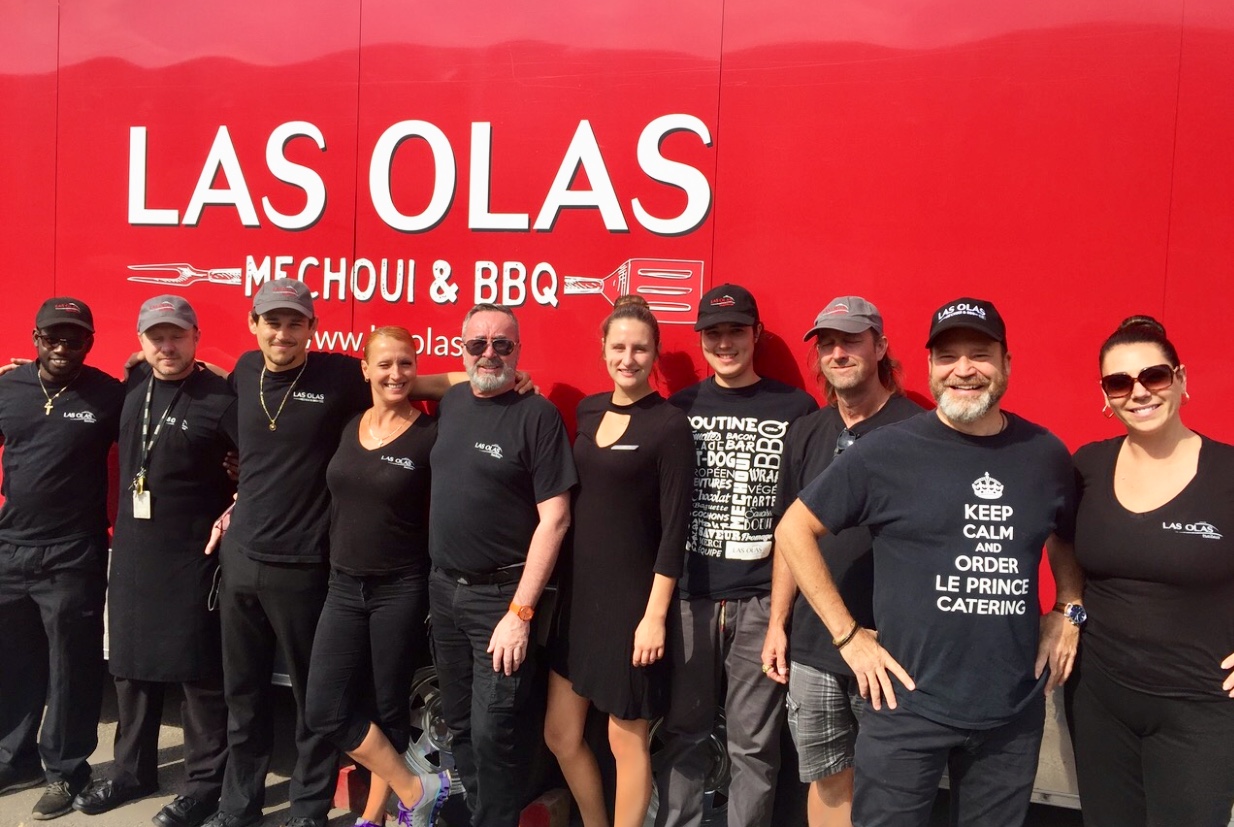 Un groupe de personnes debout devant un camion qui indique Las Olas BBQ Traiteur.