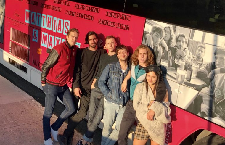 Le réalisateur Xavier Dolan et un groupe de personnes debout devant un bus rose.