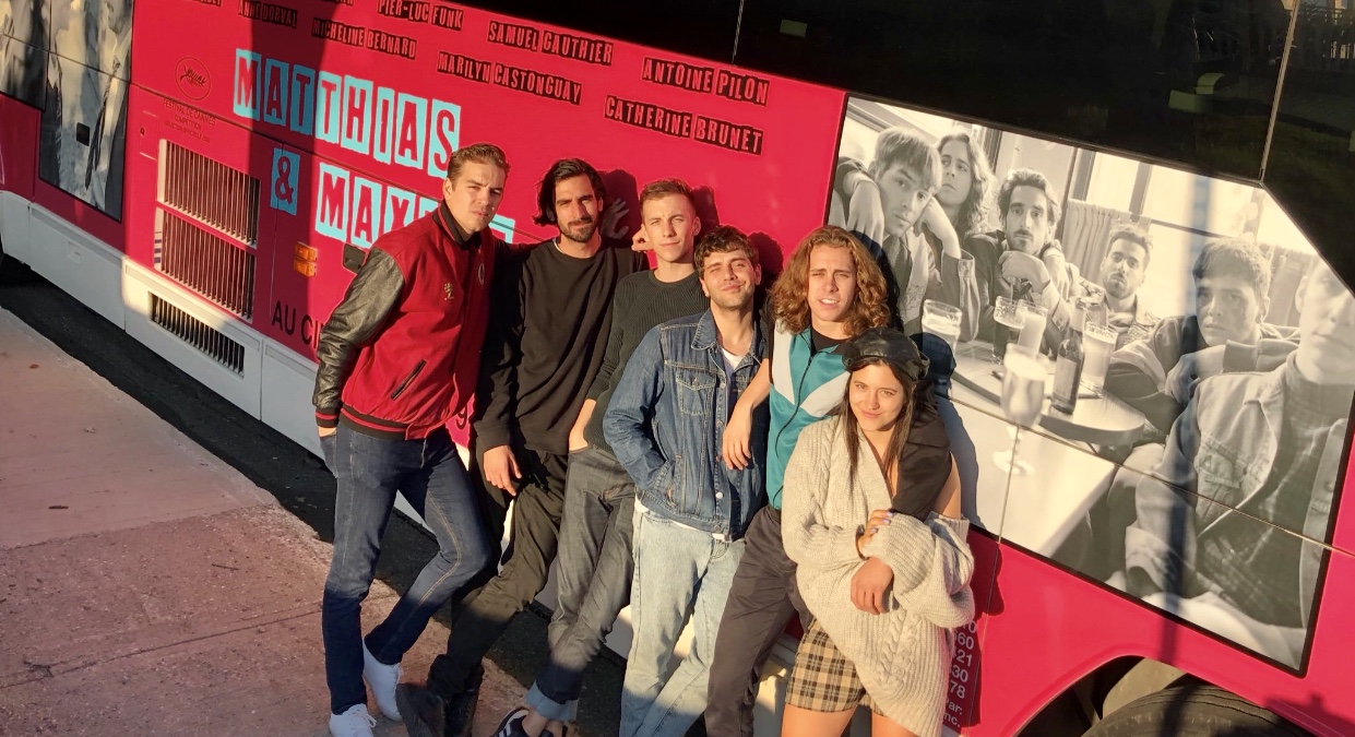Le réalisateur Xavier Dolan et un groupe de personnes debout devant un bus rose.