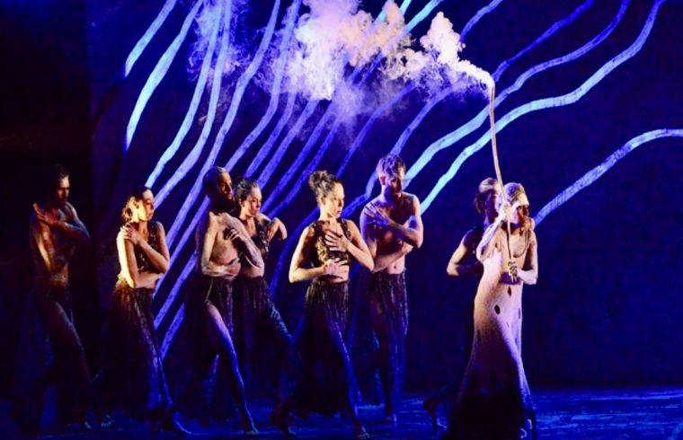 Un groupe de danseurs contemporains australiens sur scène, avec de la fumée sortant de leur bouche.