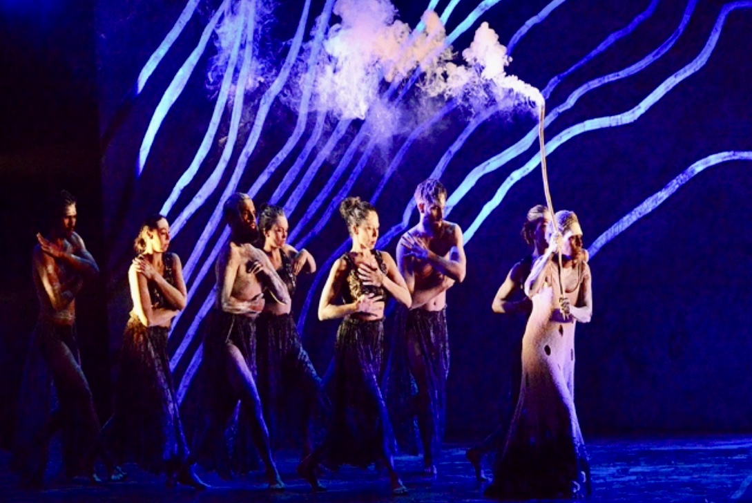 Un groupe de danseurs contemporains australiens sur scène, avec de la fumée sortant de leur bouche.