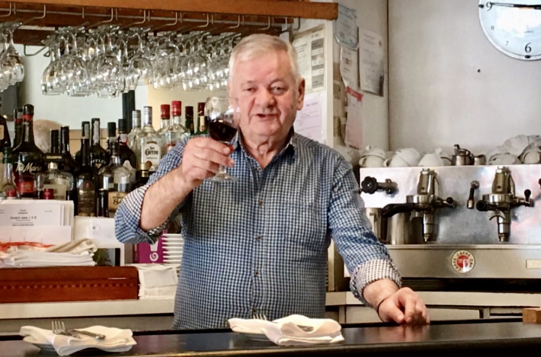 Un homme plus âgé tenant un verre de vin devant un bar à vin.