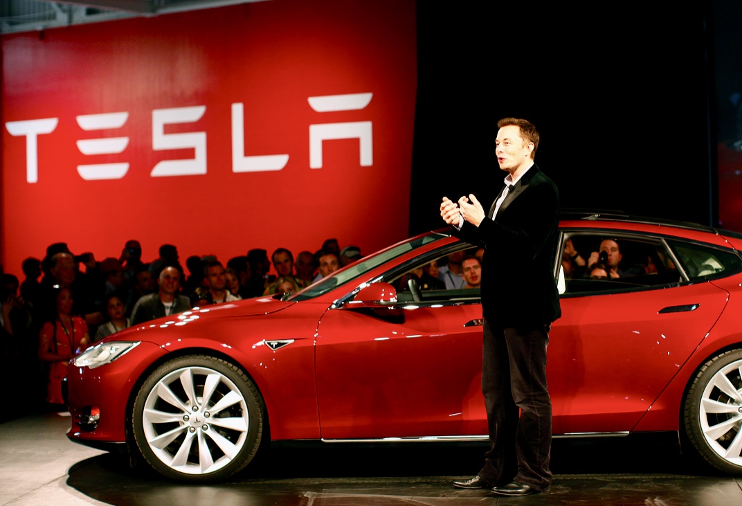 Elon Musk, le pionnier de la Révolution électrique, se tient devant une voiture Tesla.