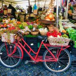 Un vélo rouge est garé devant un stand de fruits et légumes en Italie.
