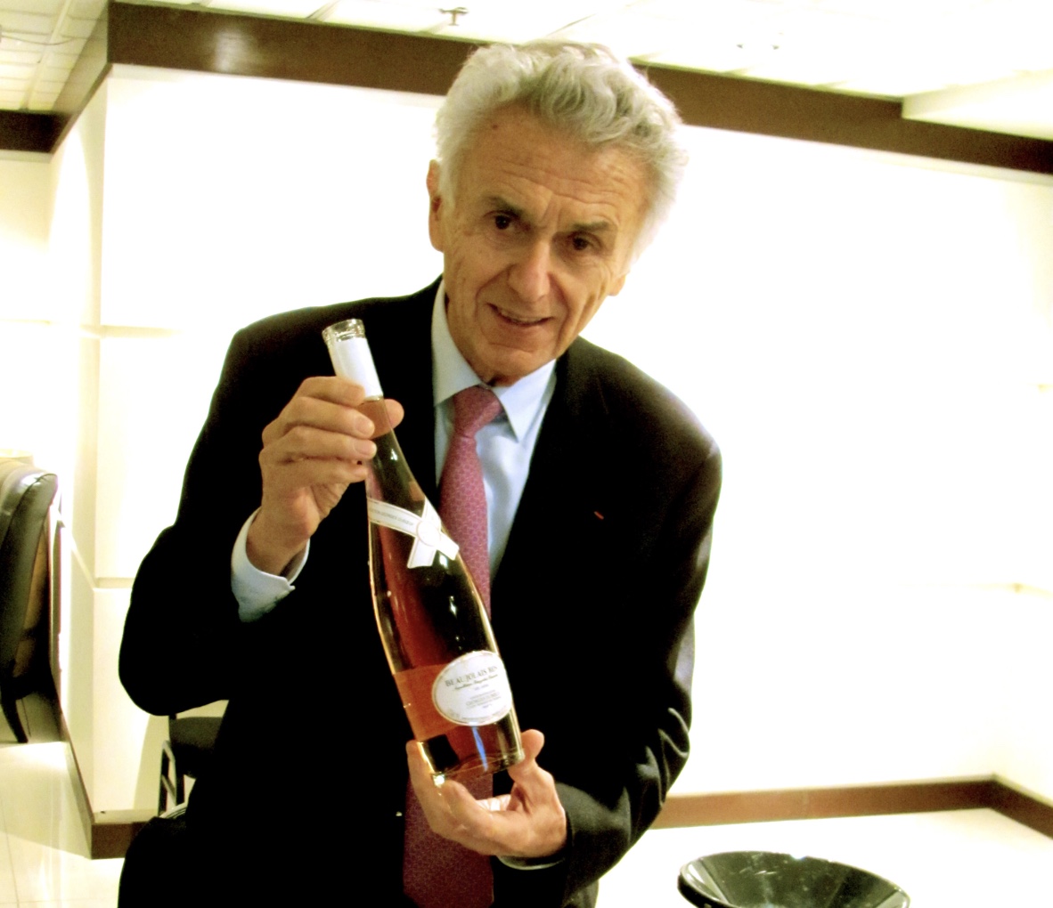 Un homme en costume tenant une bouteille de Beaujolais.