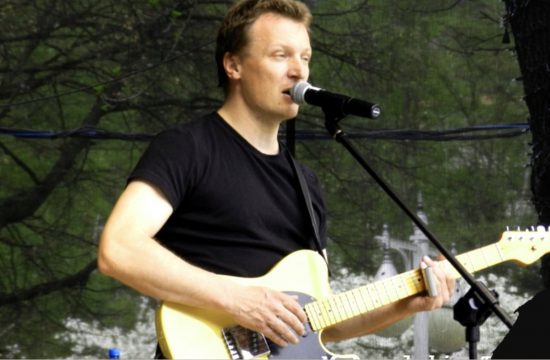 Andrzej Bachleda jouant de la guitare électrique devant un microphone.