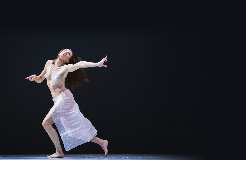 Une femme en robe blanche danse avec grâce et fluidité sur fond noir, mettant en valeur ses prouesses en danse contemporaine.