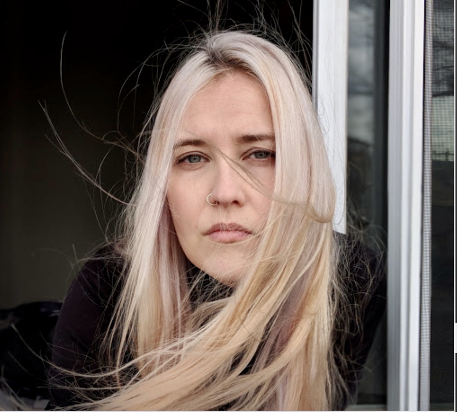 Une femme avec une longue chevelure blonde, adossée à une fenêtre.