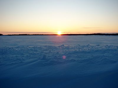 Le soleil se couche sur un champ de toundra couvert de neige.